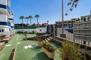 A rooftop terrace with green flooring, potted plants, and a view of palm trees and buildings. - GuestReady - Bello Horizonte Sea View and Pool (San Bartolomé de Tirajana)