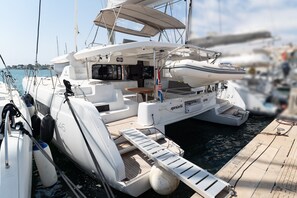 A white yacht docked at a marina with a covered seating area, a small table, and a flag. - Sun-Kissed Sailing Adventure in Islas Baleares, Mallorca (Portocolom)