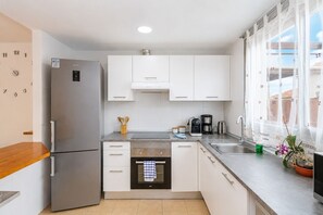 A modern kitchen with white cabinets, stainless steel appliances, and a window with sheer curtains. - GuestReady - Villa with Pool and Terrace (Costa Teguise)