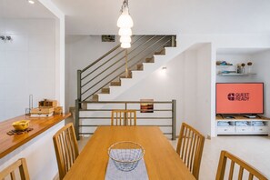 A modern kitchen with a wooden dining table, chairs, a hanging light fixture, a staircase, and a television displaying 'GUEST READY'. - GuestReady - Villa with Pool and Terrace (Costa Teguise)