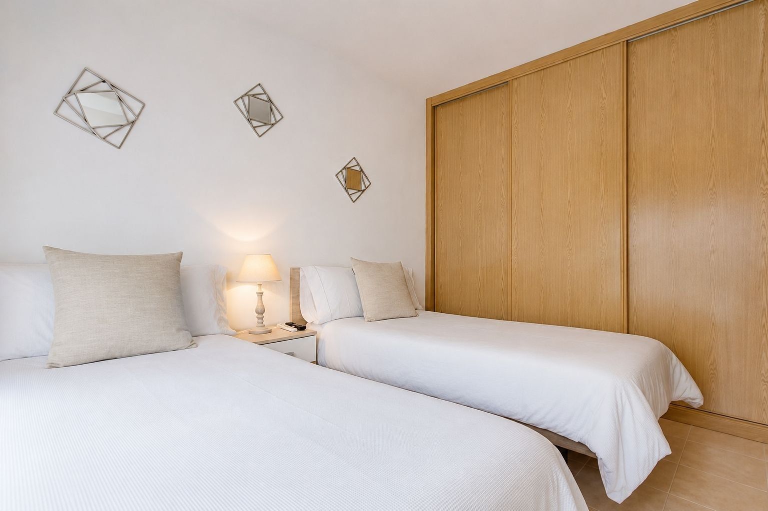 A hotel room with two beds, a nightstand with a lamp, and a wooden wardrobe.