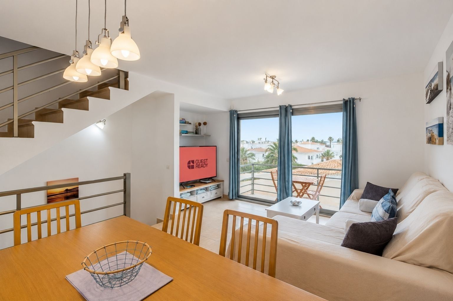 Un salon moderne avec un canapé, une table à manger et un téléviseur. Il y a un balcon avec vue sur la ville.
