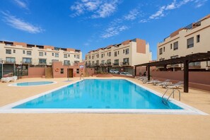 A swimming pool with lounge chairs and a covered area, surrounded by apartment buildings. - GuestReady - Villa with Pool and Terrace (Costa Teguise)