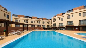 Ein Schwimmbecken mit Liegestühlen und einer Pergola, umgeben von mehrstöckigen Gebäuden mit Balkonen.
