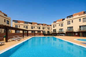 A swimming pool with lounge chairs and a pergola, surrounded by multi-story buildings with balconies. - GuestReady - Villa with Pool and Terrace (Costa Teguise)
