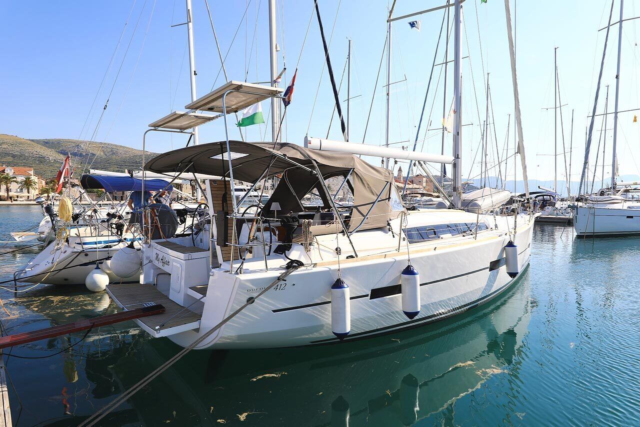 Un voilier est amarré dans une marina, doté d’une terrasse couverte, de plusieurs mâts et offrant une vue dégagée sur l’eau et les bâtiments environnants.