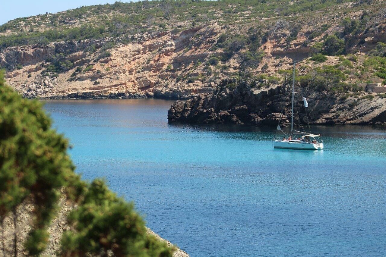 A boat on a calm body of water with rocky cliffs in the background.