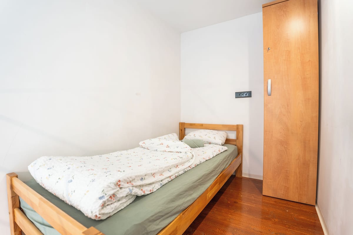 Una cama individual con colcha estampada, cabecera de madera y protector de colchón verde.
