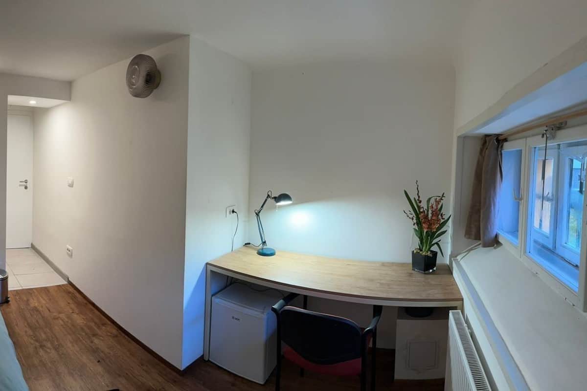Una habitación pequeña con cama, mesita de noche, escritorio y silla, además de un radiador.