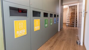 A hallway with recycling bins labeled for plastic, glass, and other materials.