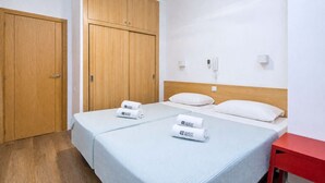 Ein Hotelzimmer mit zwei Betten, einem Holzschrank, einem roten Nachttisch und einem Deckenventilator.