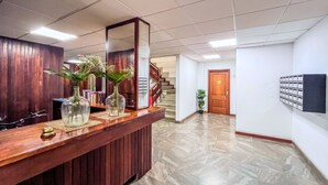 Ein Empfangsbereich mit einer Holztresen, einem großen Spiegel und zwei Vasen mit Blumen. Im Hintergrund führt eine Treppe zu einer weiteren Etage.