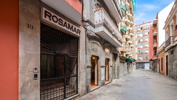 Eine schmale Straße mit einem Gebäude, an dem 'ROSAMAR' steht, mit einem großen Metallgitter und einem kleinen Eingang.