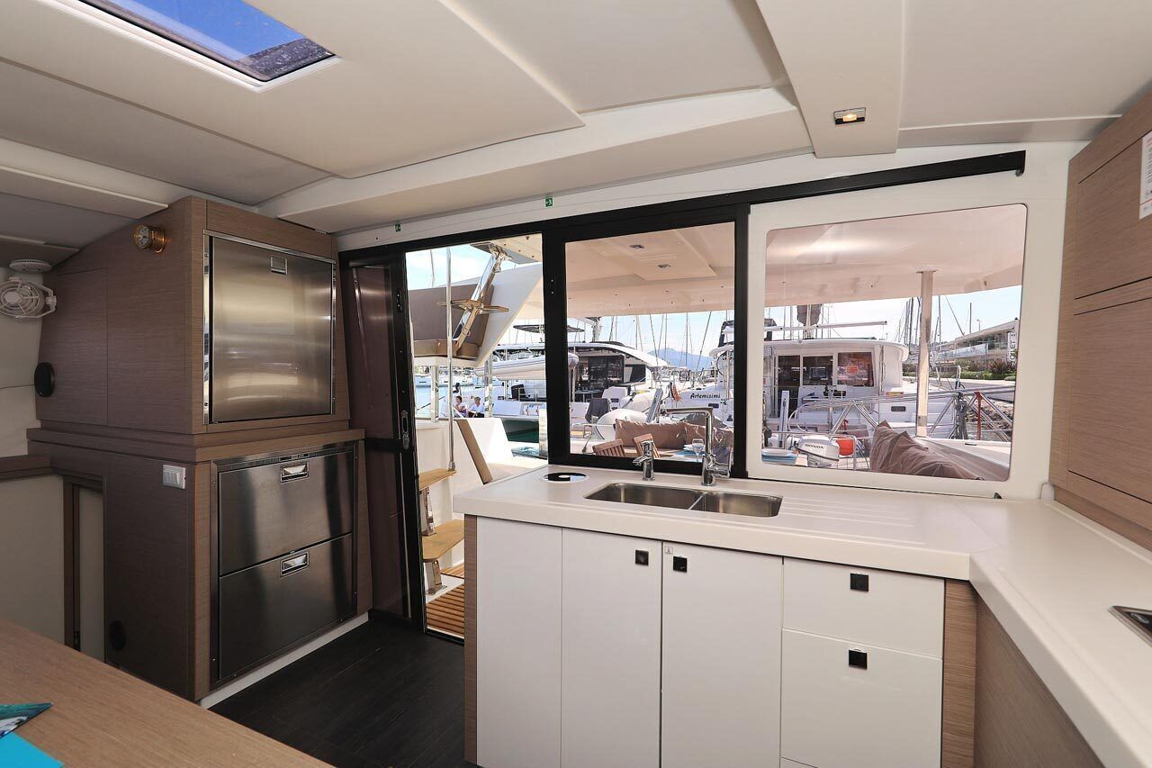 A compact kitchen with stainless steel appliances, a window with a view of boats, and a small seating area.