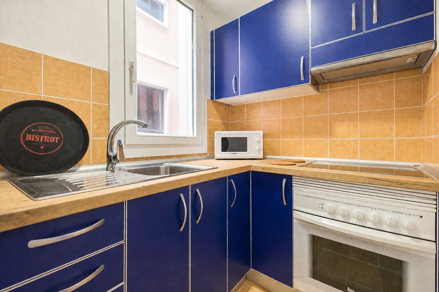 Una cocina con gabinetes azules, un microondas blanco, una estufa y un ventanal.