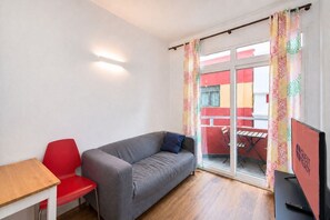Ein Zimmer mit grauem Sofa, rotem Sessel, Holztisch und Fernseher.