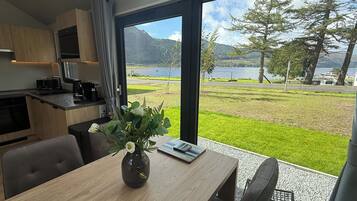 A modern kitchen with a large window, a dining table with a vase, and a view of a lake and mountains.