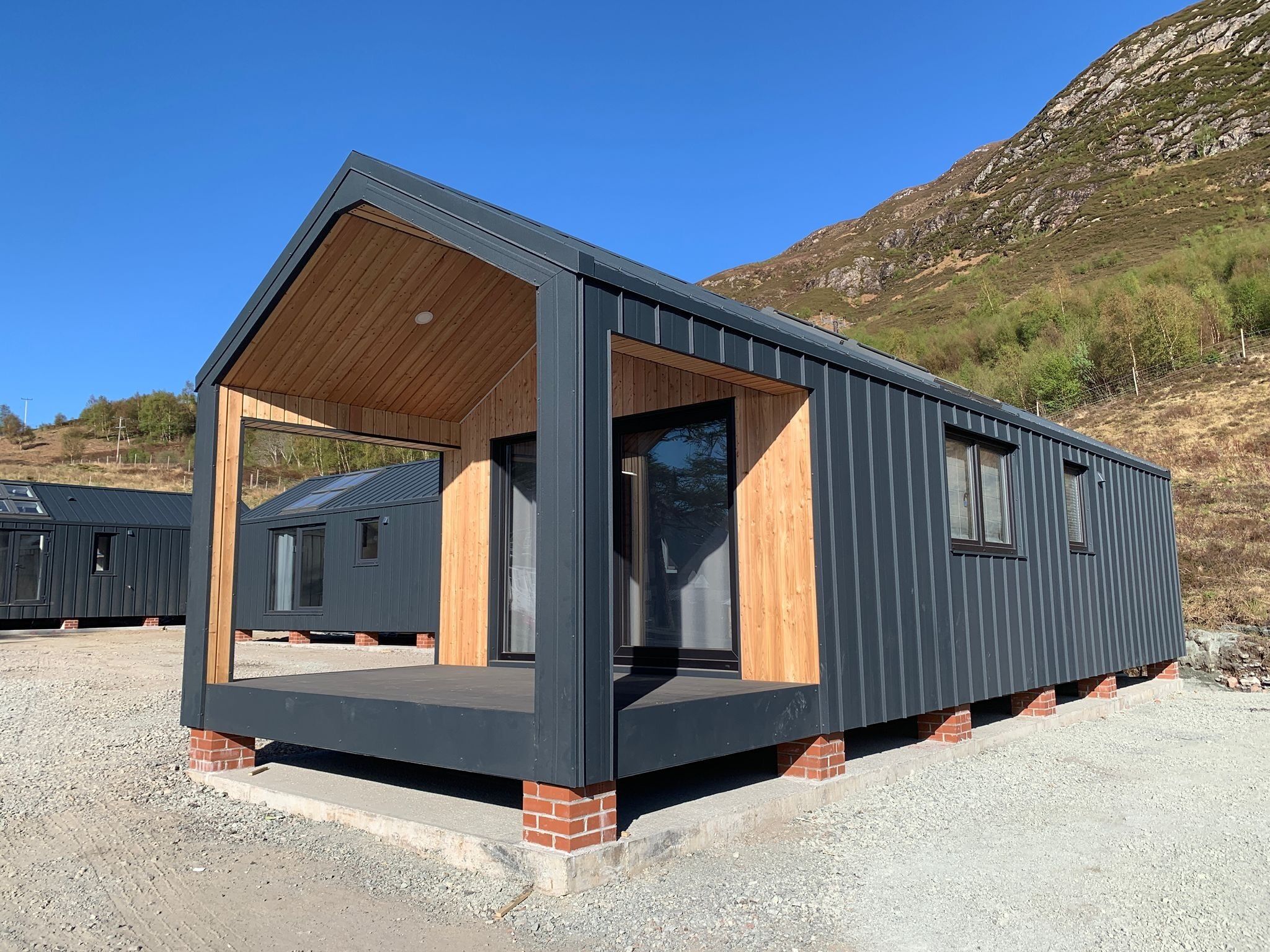 Une cabane moderne de plain-pied, dotée d’un toit en pente, de grandes fenêtres et d’une véranda en bois.