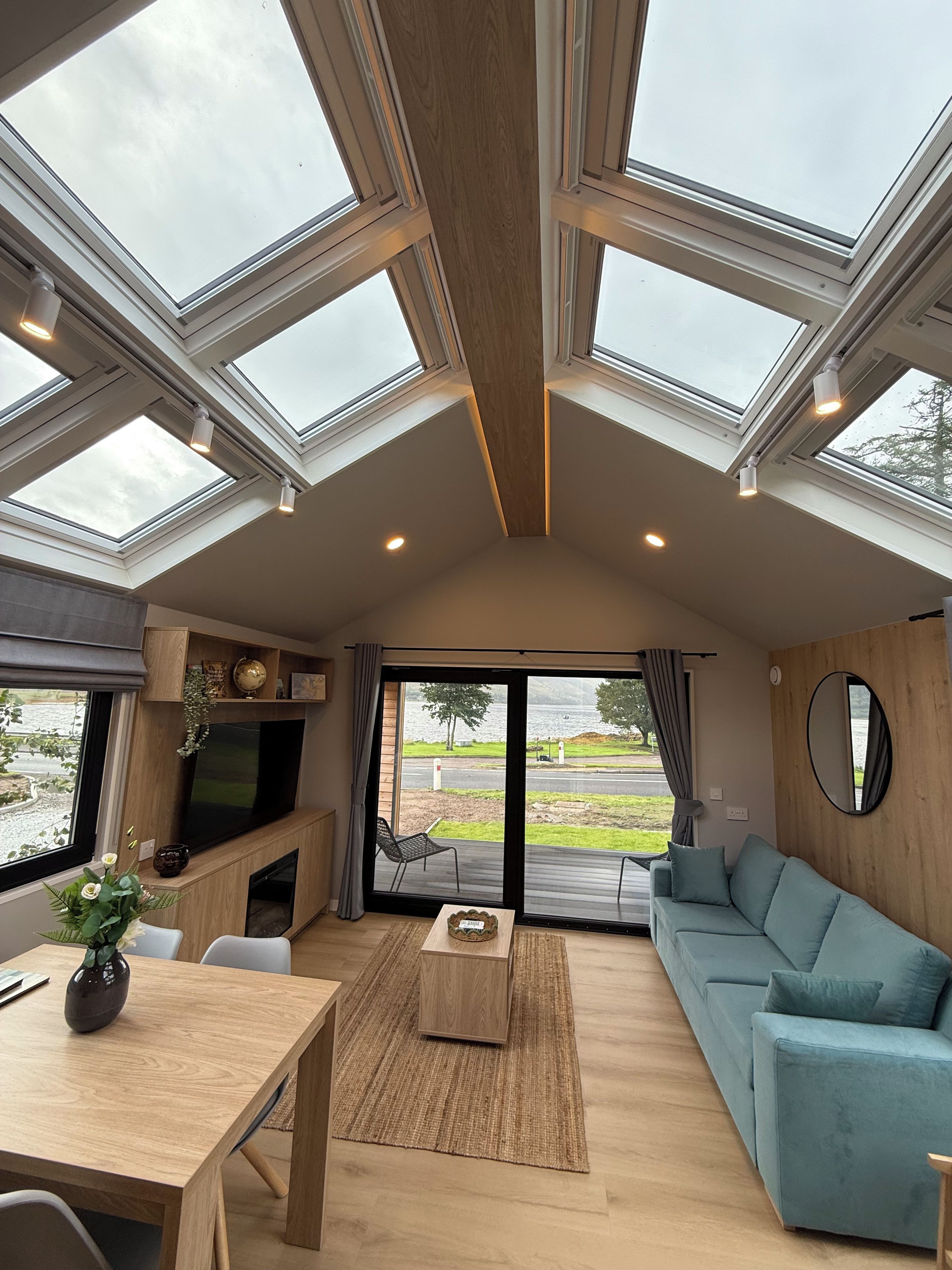 A modern living room with a large skylight, a flat-screen TV, a sofa, and a dining table.