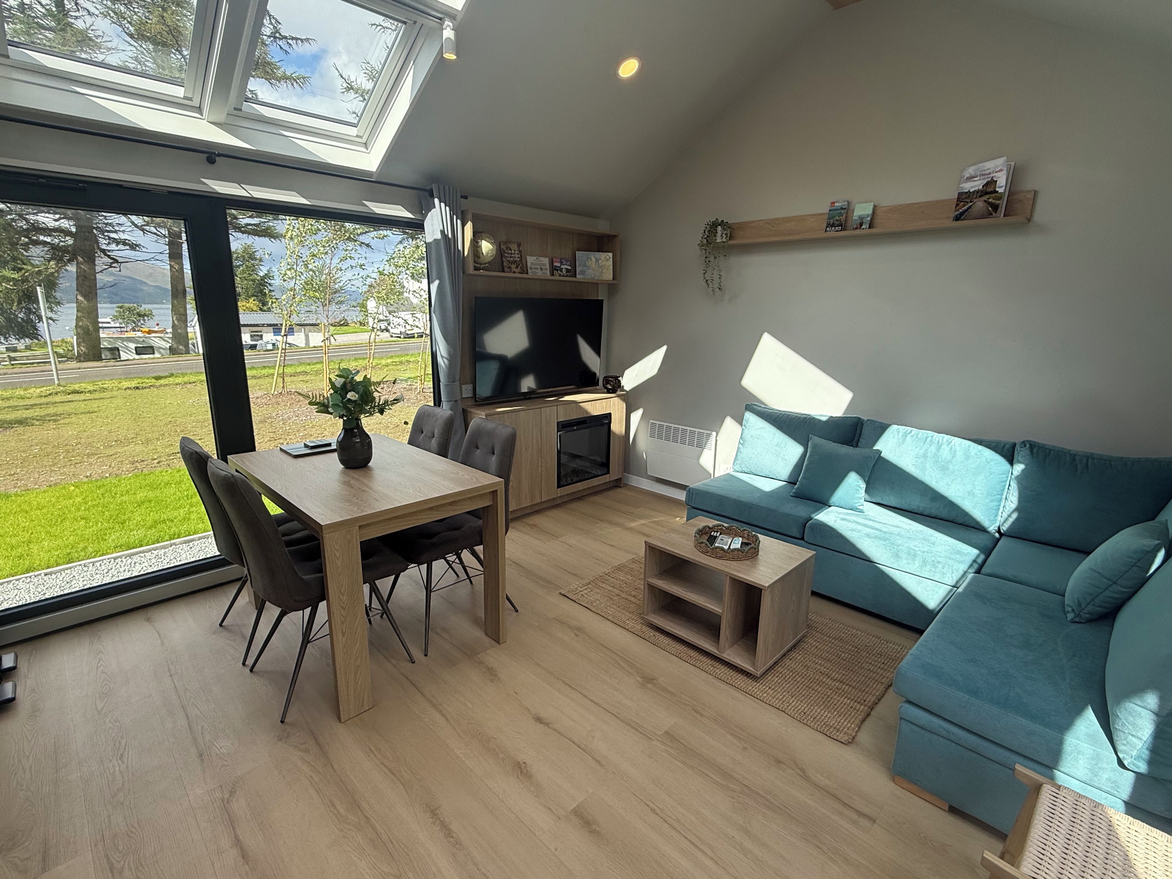 A modern living space with a dining area, sofa, and a large window overlooking a grassy area.