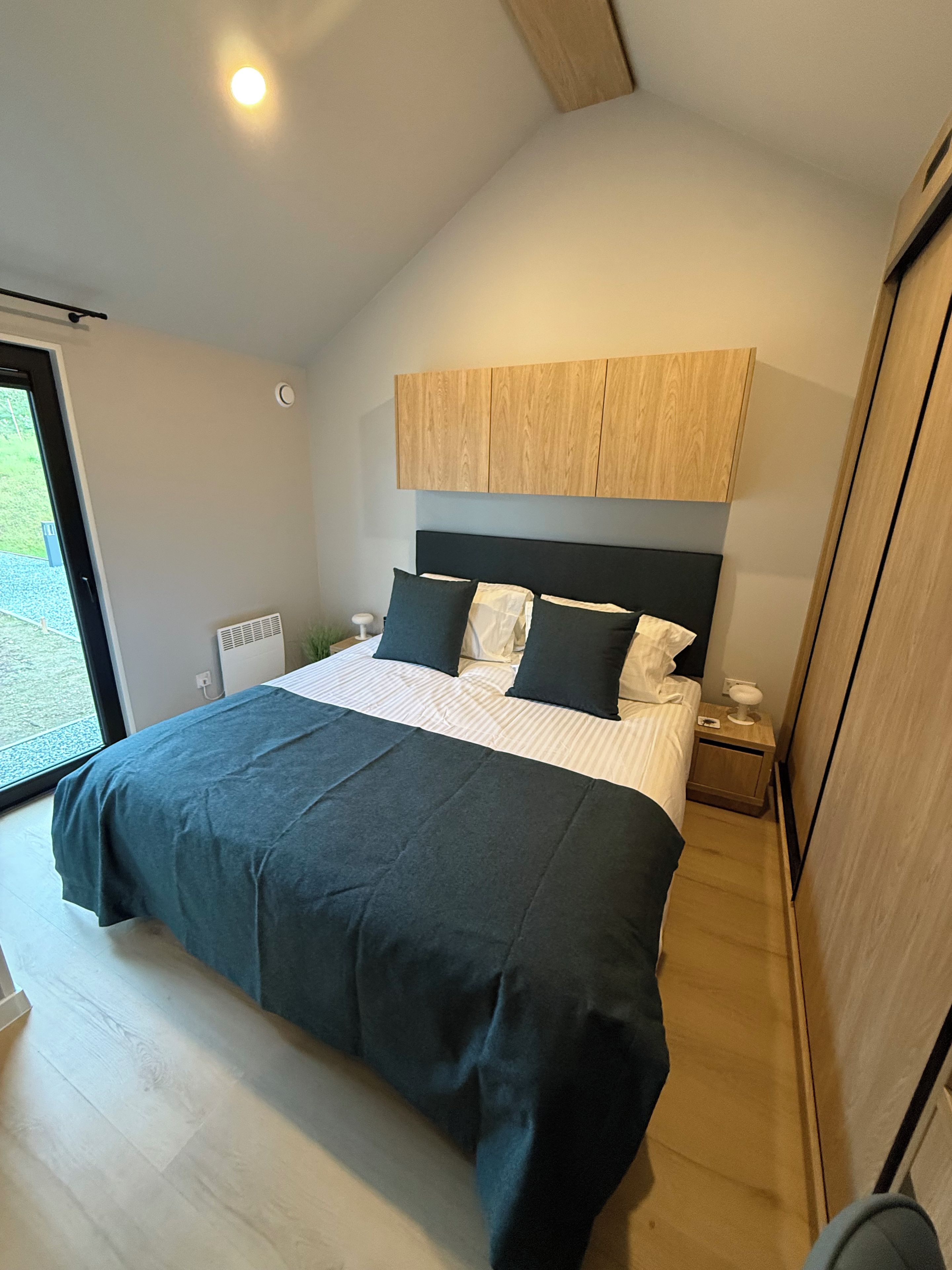 Un dormitorio moderno con una cama grande, cabecera de madera y vistas al exterior a través de un ventanal.