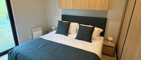 Un dormitorio moderno con una cama grande, cabecera de madera y vistas al exterior a través de un ventanal.