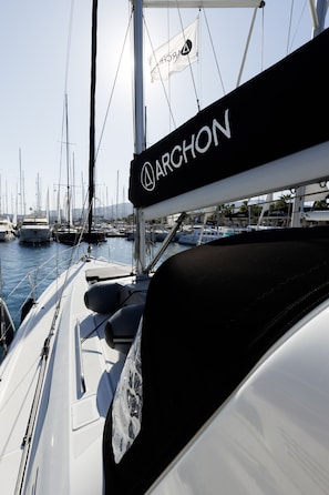 A marina with multiple boats docked, a sailboat with 'ARCHON' branding, and a clear sky. - Sun-Kissed Sailing Adventure in the Dodecanese Islands (Kos)