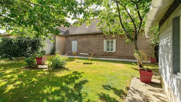 A brick house with a lawn, a table, and chairs outside.