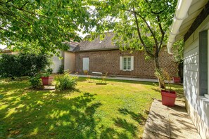 A brick house with a lawn, a table, and chairs outside.