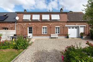 A two-story brick house with a gravel driveway, a bench, and potted plants.