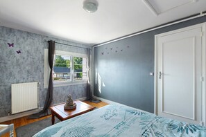 A bedroom with a bed, a radiator, a window with curtains, a door, and butterfly wall decals.
