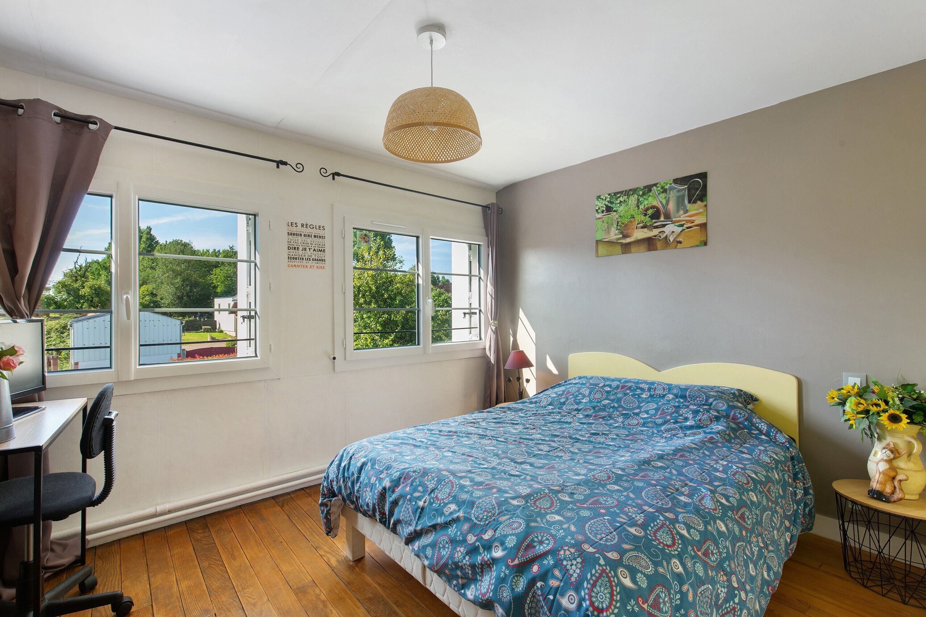 Une chambre à coucher avec un lit, un bureau, une chaise, une lampe et une fenêtre avec des rideaux.