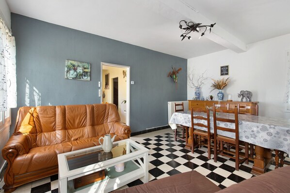 A living room with a brown leather sofa, a glass coffee table, a dining table with chairs, and a black and white checkered floor.