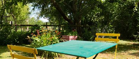 Une table de pique-nique verte avec des chaises jaunes, située dans un espace extérieur verdoyant, agrémenté d’arbres et de fleurs.