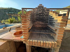 Ein gemauerter Grill im Freien mit einem Metallrost, einer Steinwanne und einem Bereich am Pool.