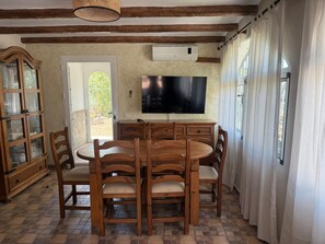 Ein Essbereich mit einem runden Holztisch, sechs Stühlen, einem an der Wand befestigten Fernseher und einem Fenster mit Vorhängen.