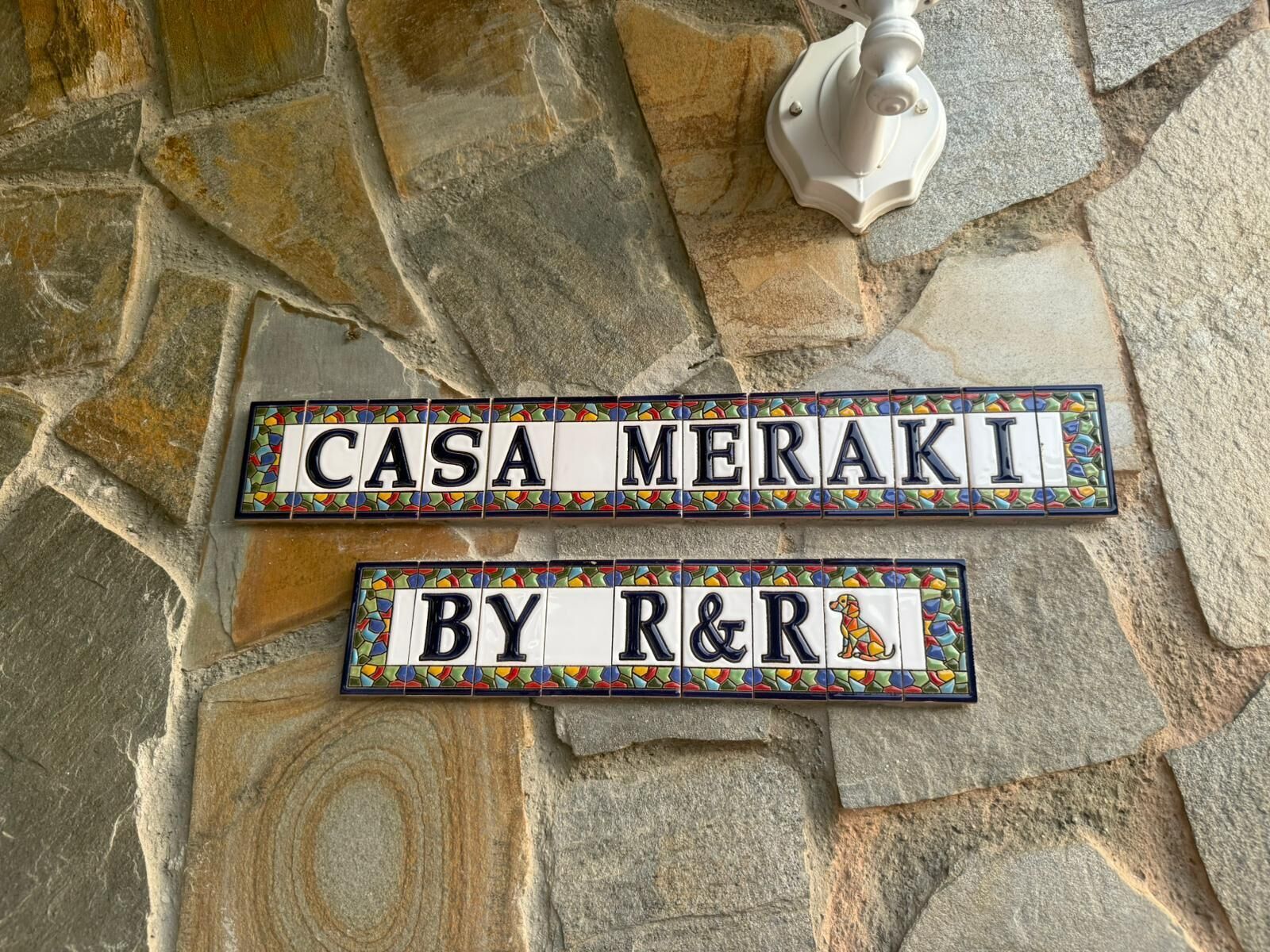 Dos placas en una pared de piedra, una que dice 'CASA MERAKI' y la otra 'BY R&R'.