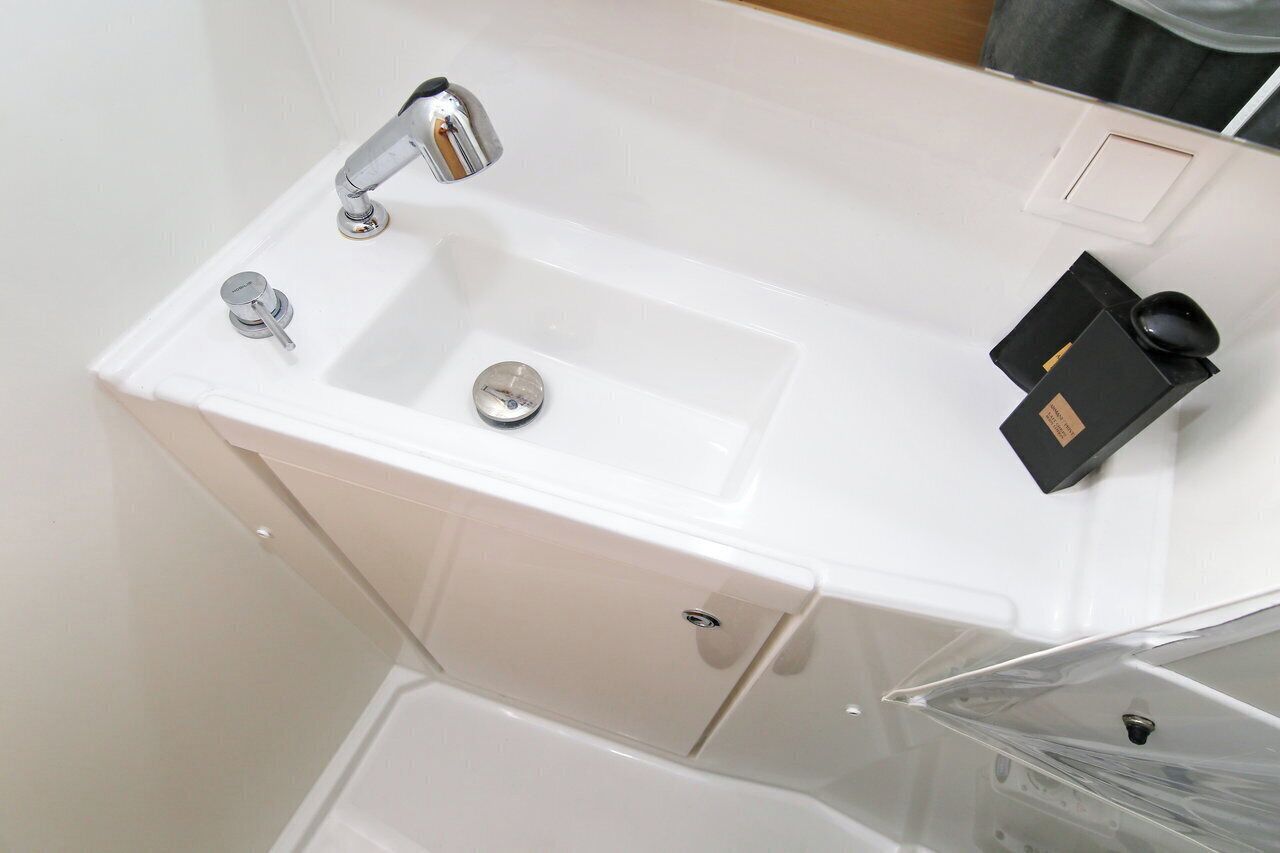 A white bathroom with a sink, faucet, and a small black object on the counter.