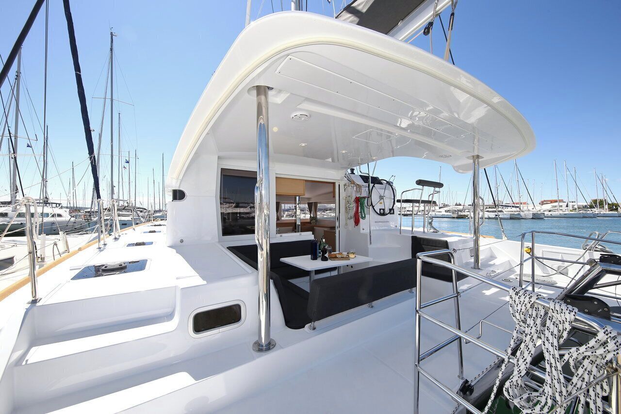 Das Deck einer Yacht mit einer überdachten Sitzecke, einem kleinen Tisch und Blick auf andere Yachten in der Marina.