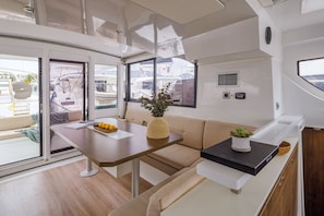 A modern interior with a dining area, a sofa, and a view of boats through large windows. - Sun-Kissed Sailing Adventure in the Saronic Islands (Nea Peramos)