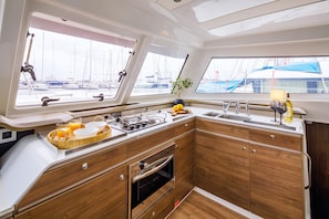 A yacht's galley with a stove, sink, and a view of the marina. - Sun-Kissed Sailing Adventure in the Saronic Islands (Nea Peramos)