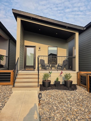 A residential building with a covered porch, a door marked '49F', and outdoor seating.