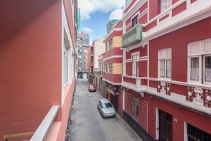 A narrow street between buildings with balconies, a parked car, and a visible sign on a building. - GuestReady - Rosamar 103 M (Las Palmas de Gran Canaria)