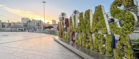 A large outdoor sign with greenery, a paved area, and buildings in the background.