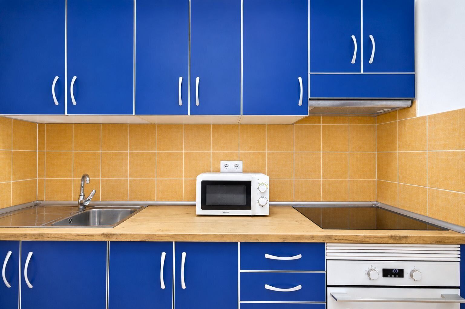 A kitchen with blue cabinets, a white microwave, a sink, and a stove.