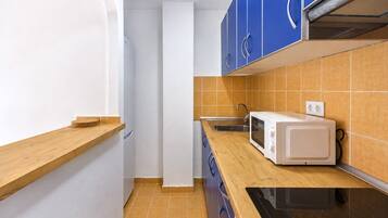 Cocina compacta con microondas, lavabo y encimera de madera.