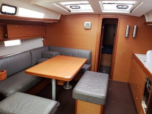 A compact galley with a wooden table, grey cushioned seating, a small cabinet, and a window. - Sun-Kissed Sailing Adventure in Islas Baleares, Mallorca (Palma)