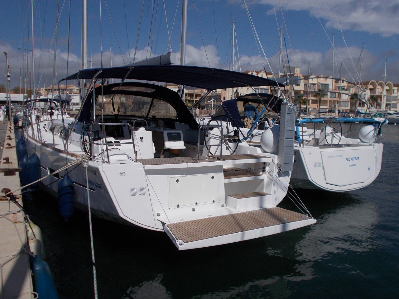 A white yacht docked at a marina with a covered deck and a visible website address.