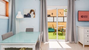 Quarto de hotel moderno com mesa de jantar de vidro, sofá, quadro, porta de vidro deslizante para o jardim e um aviso com a inscrição 'GUEST READY'.