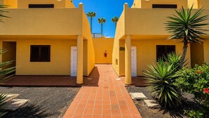 Um pátio com edifícios amarelos, um caminho de azulejos e algumas plantas.